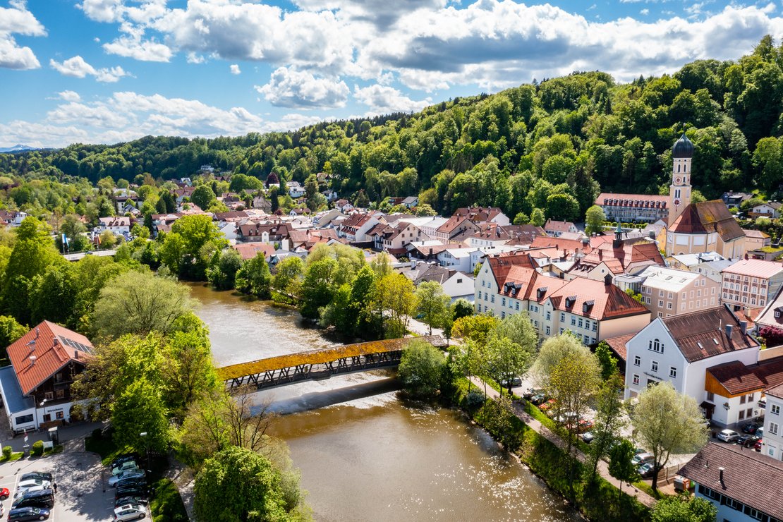 Ein Fluss fließt duch eine kleine Stadt, im Hintergrund grüne Hügel.