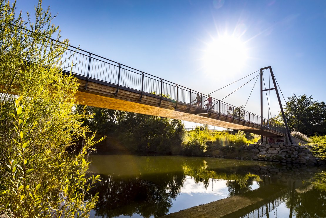 Eine Brücke, auf der Fahräder fahren, spannt über einen Fluss.